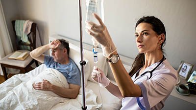 Мужчина лежит на кровати, медсестра готовит капельницу